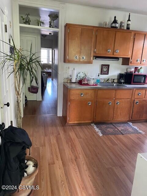 kitchen featuring a sink, brown cabinets, dark countertops, and wood finished floors