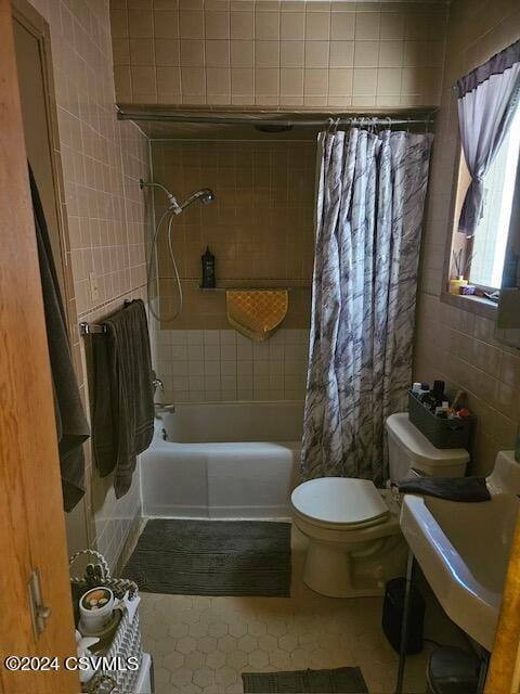 full bathroom with a sink, toilet, tile walls, and shower / tub combo with curtain