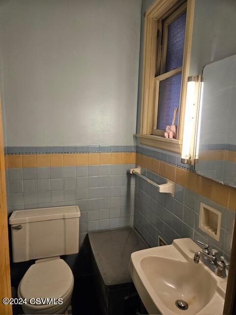 bathroom featuring a sink, a wainscoted wall, toilet, and tile walls