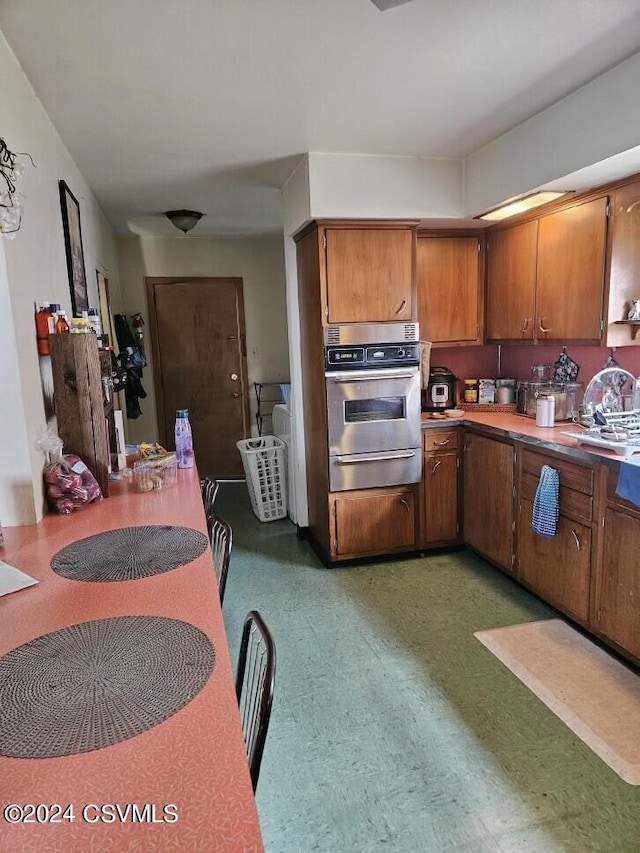 kitchen with brown cabinetry, light floors, a warming drawer, and stainless steel oven