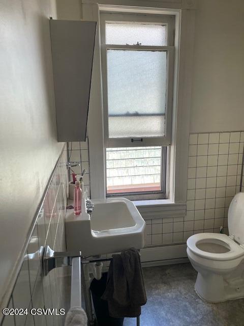 half bath featuring tile walls, toilet, a wealth of natural light, and a sink