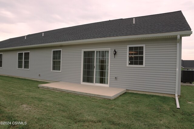 back house at dusk with a patio area, central AC, and a yard