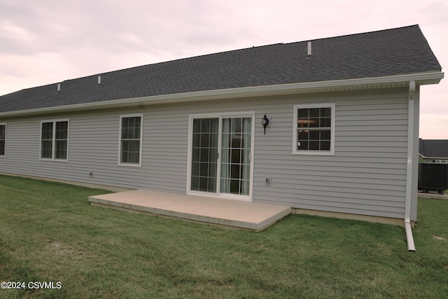 rear view of house featuring roof with shingles, cooling unit, a lawn, and a patio