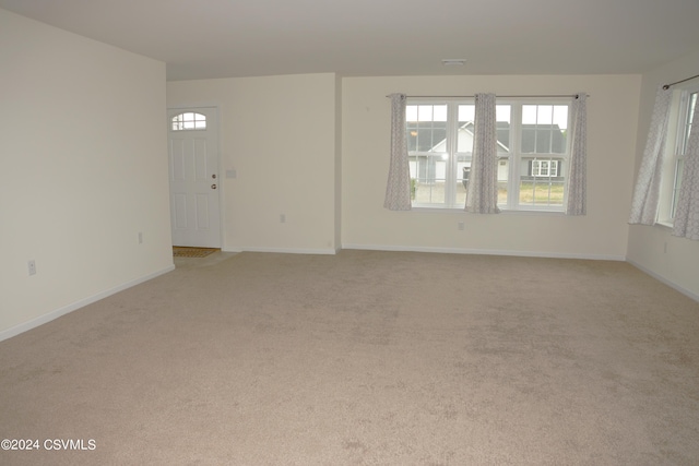 spare room featuring light carpet, plenty of natural light, and baseboards