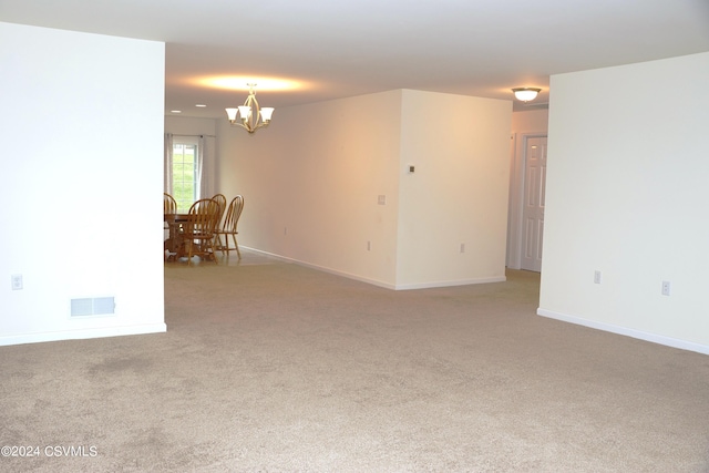 empty room featuring light carpet, baseboards, visible vents, and a notable chandelier