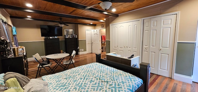 bedroom featuring ceiling fan, hardwood / wood-style flooring, multiple closets, wooden ceiling, and beam ceiling