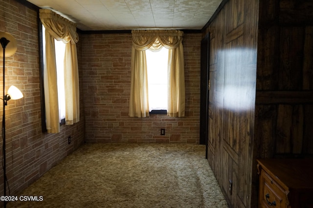 carpeted empty room featuring brick wall