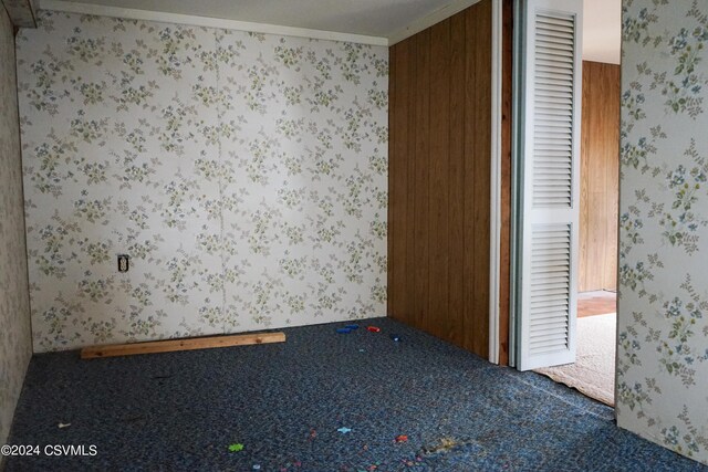 unfurnished bedroom featuring carpet, wood walls, and crown molding