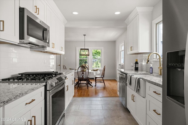 kitchen featuring appliances with stainless steel finishes, white cabinetry, hanging light fixtures, and plenty of natural light