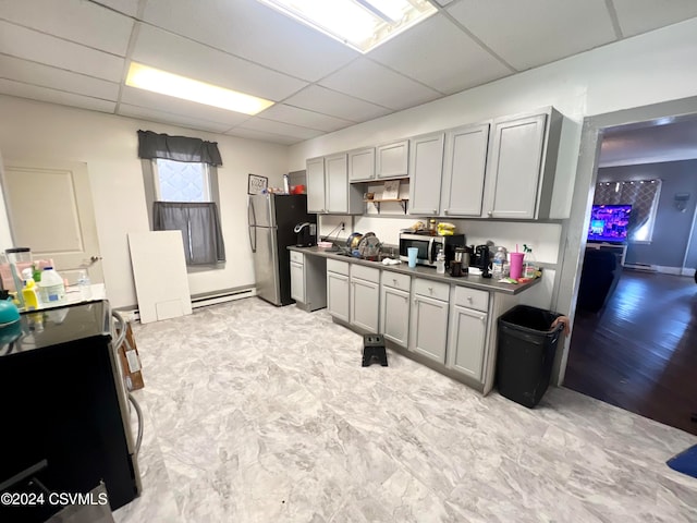 kitchen featuring a drop ceiling, light tile patterned floors, a baseboard heating unit, gray cabinets, and appliances with stainless steel finishes