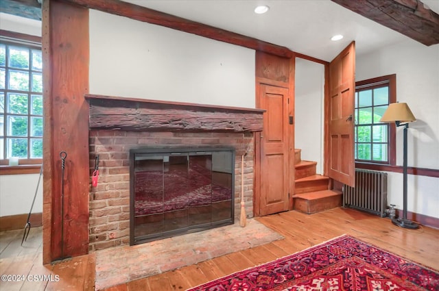 interior details with a brick fireplace, hardwood / wood-style flooring, radiator, and beamed ceiling