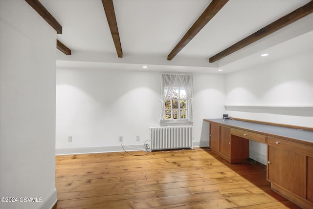 unfurnished office featuring beam ceiling, radiator heating unit, and light hardwood / wood-style flooring