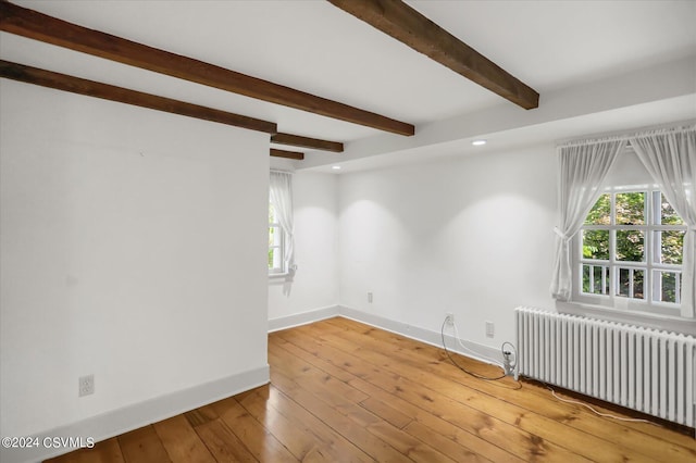 spare room with radiator, light wood-type flooring, and beamed ceiling