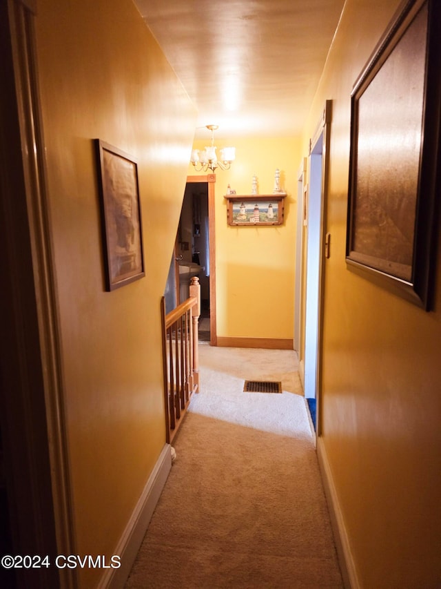 corridor with an inviting chandelier and light colored carpet