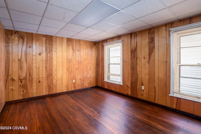 unfurnished room featuring dark wood-type flooring, a drop ceiling, and wooden walls