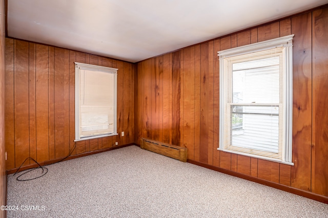 unfurnished room featuring wood walls, light colored carpet, and a baseboard radiator