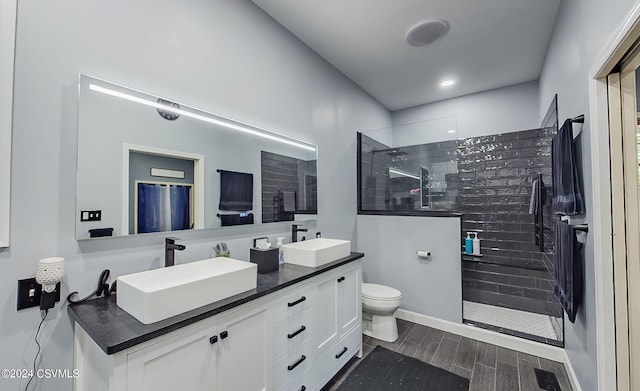 bathroom with toilet, a tile shower, and double sink vanity