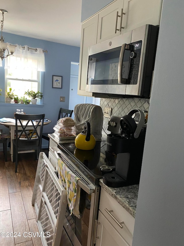 kitchen featuring backsplash, stainless steel appliances, an inviting chandelier, white cabinets, and dark wood-type flooring