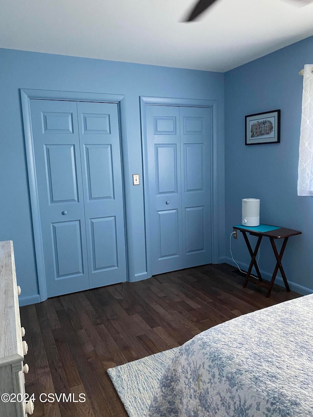 bedroom with dark hardwood / wood-style flooring, two closets, and ceiling fan