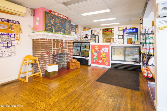 interior space with a paneled ceiling, wood-type flooring, and a wall mounted AC