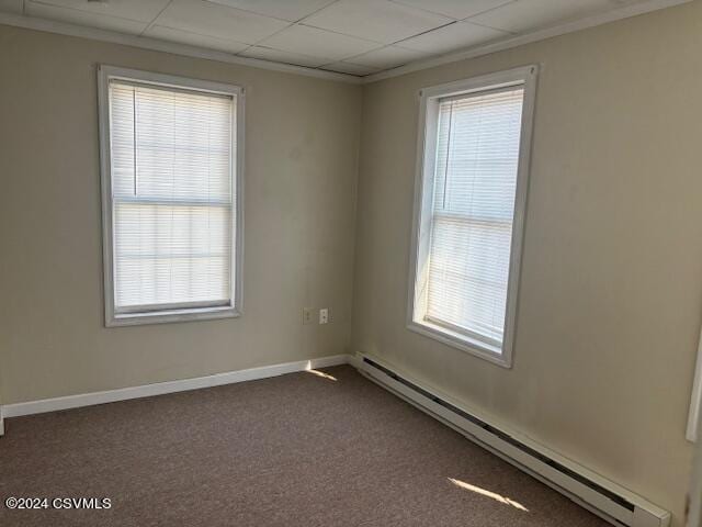 empty room with dark carpet, plenty of natural light, a paneled ceiling, and a baseboard radiator