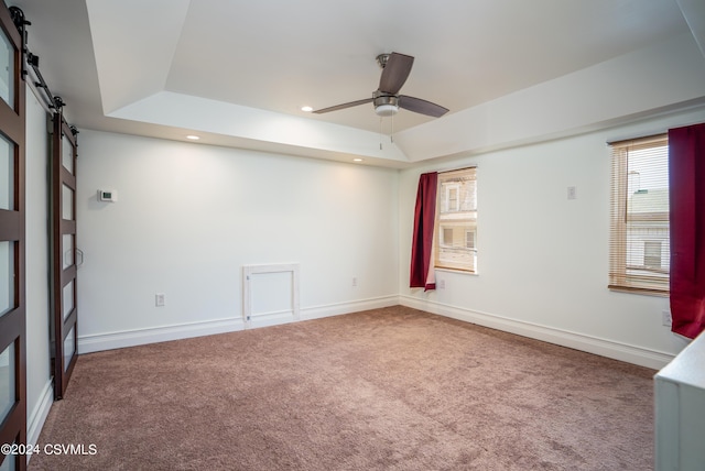 carpeted spare room featuring a raised ceiling, a barn door, plenty of natural light, and ceiling fan