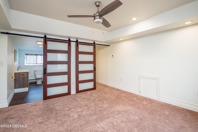 unfurnished bedroom featuring ensuite bath, a barn door, baseboard heating, and carpet flooring