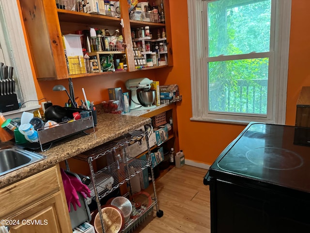 kitchen with light wood-type flooring, black range with electric cooktop, and stone counters