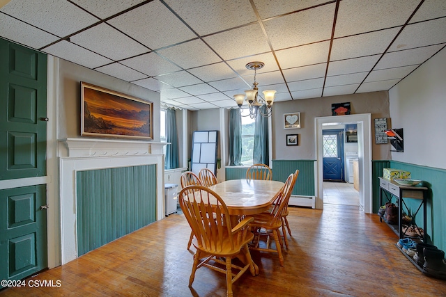 dining area with a notable chandelier, a drop ceiling, hardwood / wood-style floors, and baseboard heating