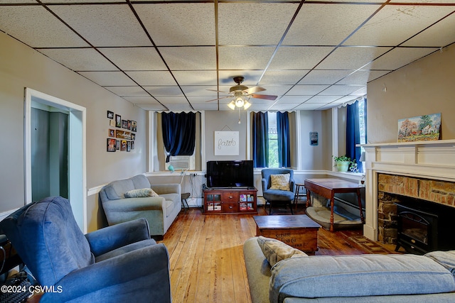 living room with ceiling fan, a paneled ceiling, hardwood / wood-style flooring, and a wood stove