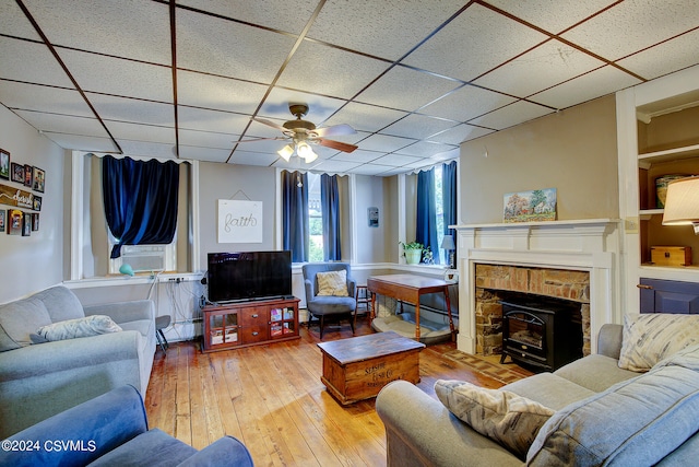 living room with a paneled ceiling, hardwood / wood-style floors, a wood stove, a fireplace, and ceiling fan