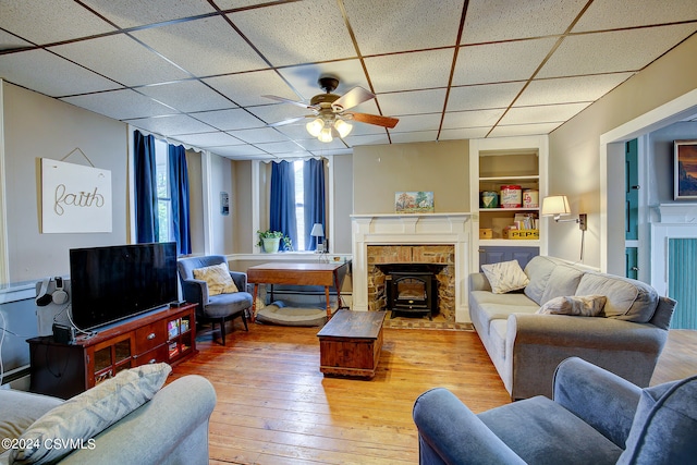 living room featuring light hardwood / wood-style floors, a drop ceiling, built in shelves, and ceiling fan