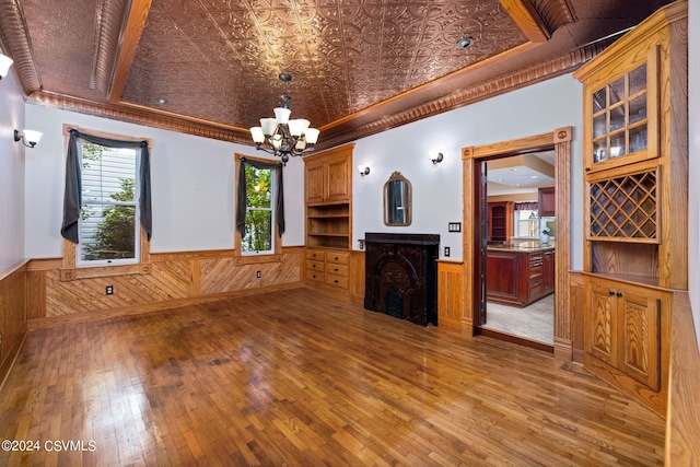 unfurnished living room featuring a raised ceiling, hardwood / wood-style flooring, an inviting chandelier, and crown molding