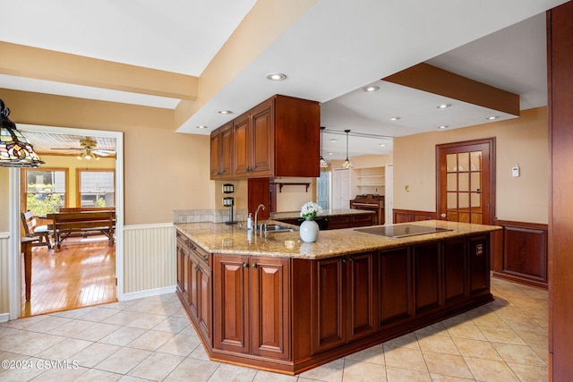 kitchen featuring black electric cooktop, light wood-type flooring, light stone countertops, kitchen peninsula, and hanging light fixtures