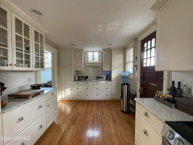 kitchen with white cabinets, a wealth of natural light, light hardwood / wood-style flooring, and backsplash