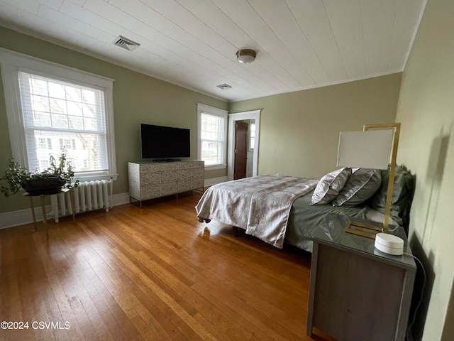 bedroom featuring radiator heating unit, wood-type flooring, and crown molding