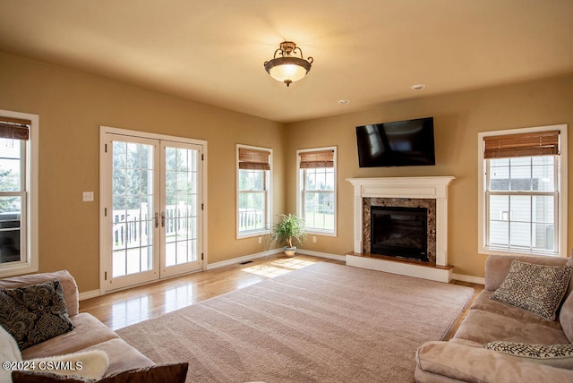 living room featuring a fireplace, light wood-type flooring, french doors, and a healthy amount of sunlight