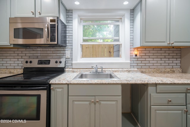 kitchen with sink, decorative backsplash, appliances with stainless steel finishes, and light stone countertops