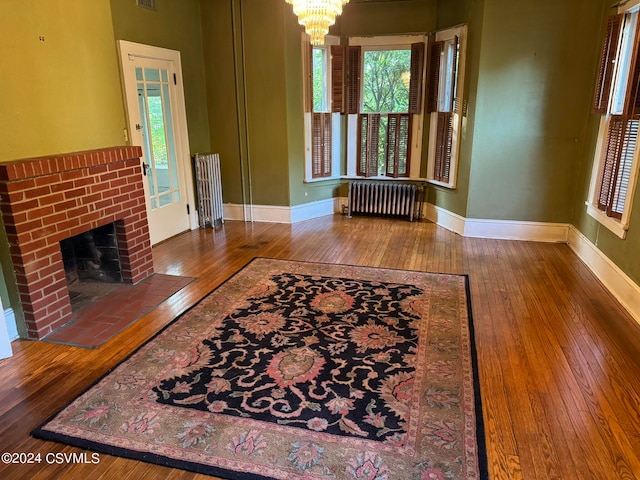 living room featuring an inviting chandelier, hardwood / wood-style floors, radiator, and a fireplace