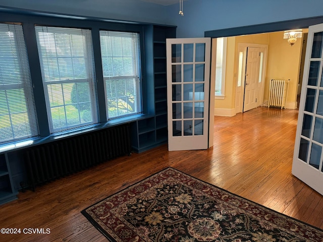 empty room featuring french doors, hardwood / wood-style flooring, and radiator heating unit