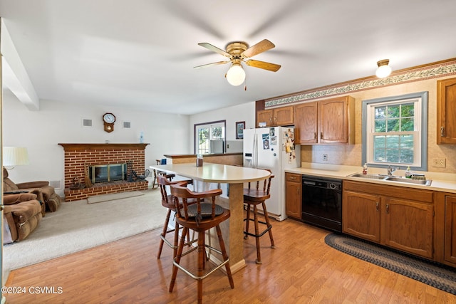 kitchen featuring white refrigerator with ice dispenser, a brick fireplace, black dishwasher, ceiling fan, and light hardwood / wood-style flooring