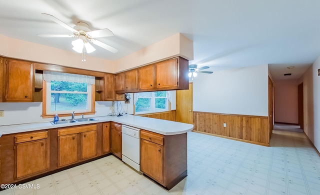 kitchen featuring kitchen peninsula, white dishwasher, ceiling fan, wooden walls, and sink