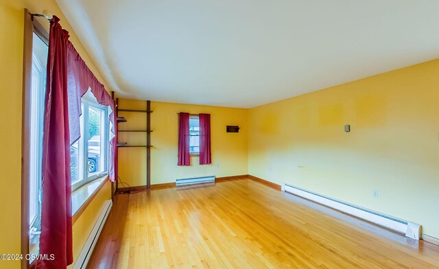 empty room with a baseboard heating unit, hardwood / wood-style floors, and a healthy amount of sunlight