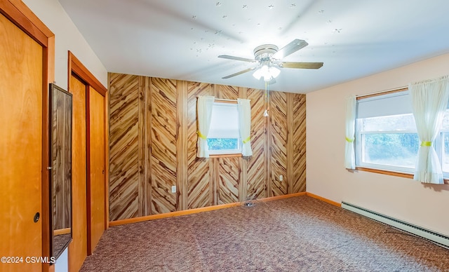 carpeted spare room featuring wood walls, baseboard heating, and ceiling fan