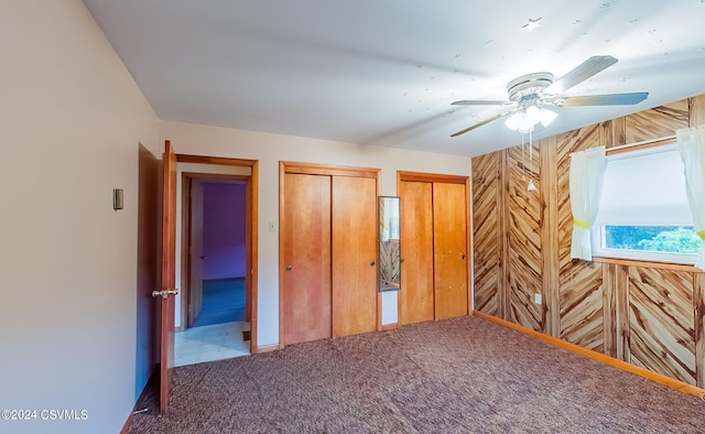 unfurnished bedroom featuring ceiling fan, wooden walls, two closets, and carpet flooring