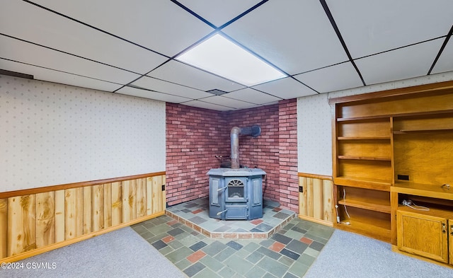 living room featuring dark tile patterned flooring, a drop ceiling, wood walls, and a wood stove