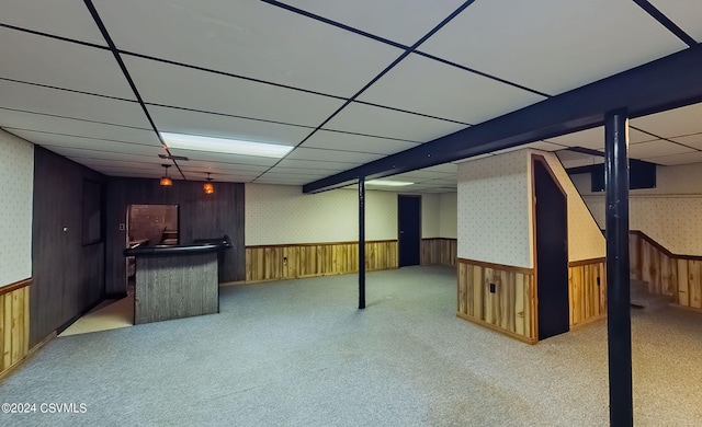 basement featuring wood walls, light colored carpet, and a paneled ceiling