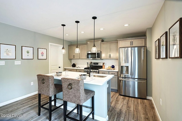 kitchen with a kitchen island with sink, dark wood-type flooring, a breakfast bar area, appliances with stainless steel finishes, and decorative light fixtures