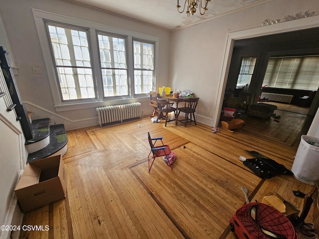 living room with wood-type flooring, ornamental molding, an inviting chandelier, and radiator heating unit