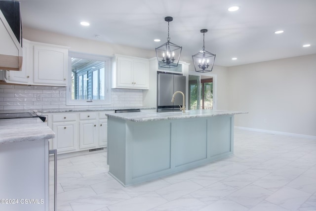 kitchen featuring white cabinets, stainless steel refrigerator, a center island with sink, and a healthy amount of sunlight